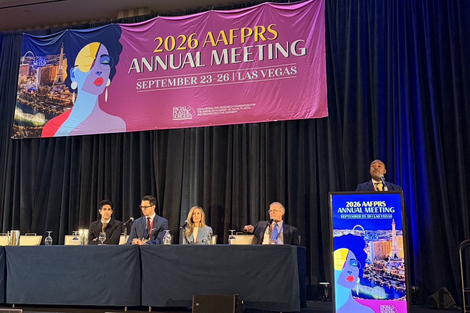 Dr. Carl Truesdale at the podium leading The Art of the Consultation panel at the 2026 AAFPRS Annual Meeting in Las Vegas, with the panelists seated beneath the AAFPRS banner
